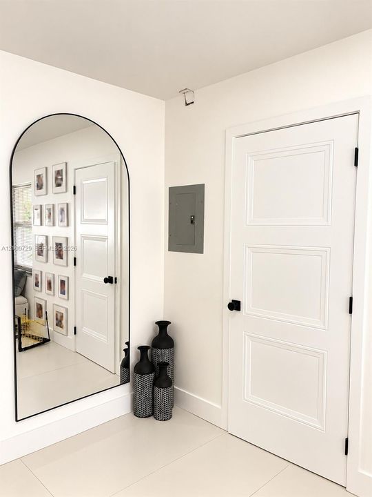 Arched wall mirror with a black metal frame, three-panel interior door with matte black hardware, and smooth-finish flooring