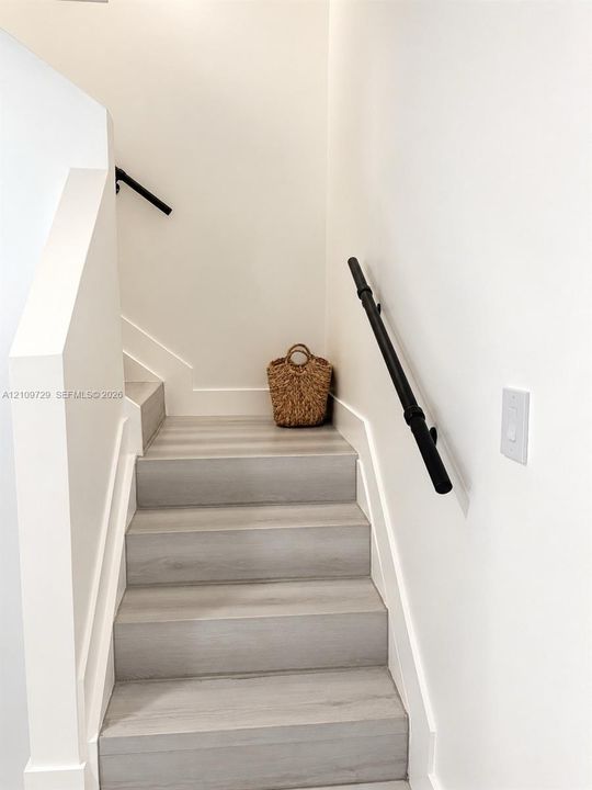 Staircase featuring wood-finish treads and matte black wall-mounted handrails
