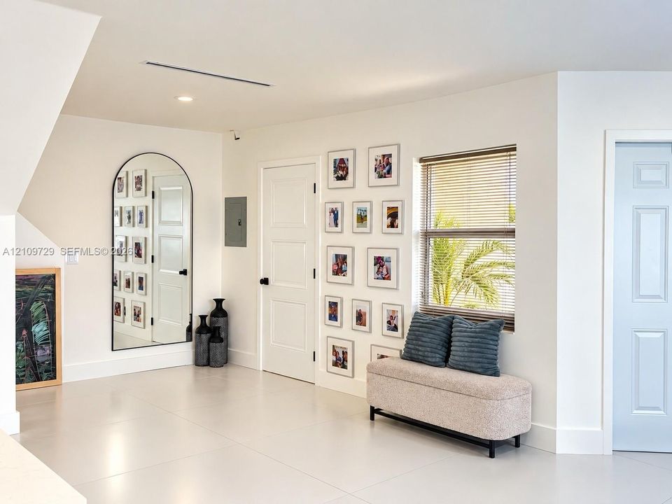 Neutral-toned tile flooring, arched wall mirror with a slender black frame, recessed ceiling lighting, and solid-core interior doors with matte black hardware