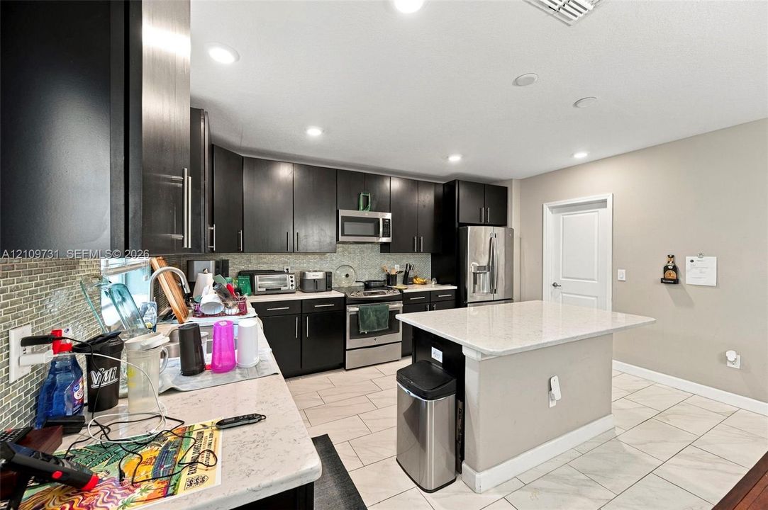 Kitchen featuring dark-finish cabinetry, stone-surface countertops, stainless steel appliances, a center island, and neutral tile flooring