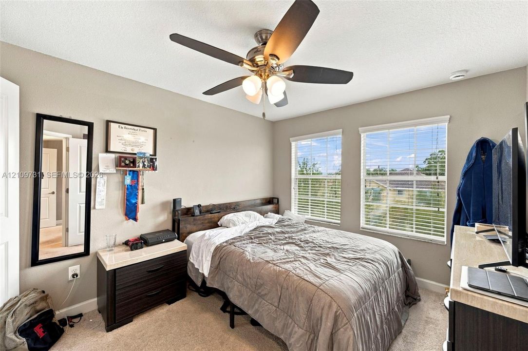 Neutral-toned interior featuring dual windows with horizontal blinds, a ceiling fan with integrated light fixture, and neutral carpeting