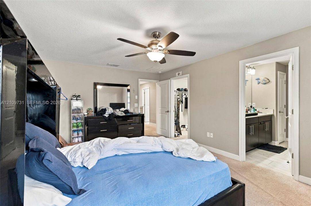 Neutral-toned interior featuring carpeted flooring, a ceiling-mounted fan with integrated lighting, and multiple interior doors providing access to a walk-in closet and bathroom