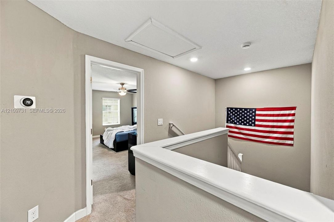 Interior landing featuring recessed ceiling lighting, a wall-mounted programmable thermostat, and a capped staircase railing