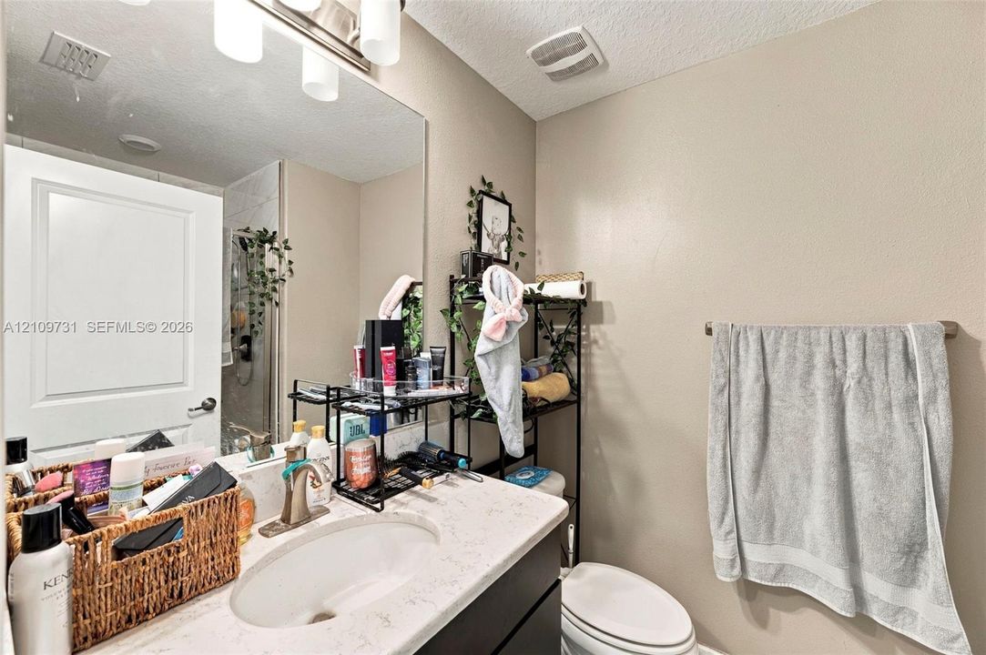 Bathroom featuring a vanity with a light-toned stone countertop, integrated oval basin, polished metal faucet, large wall-mounted mirror, and multi-bulb vanity lighting