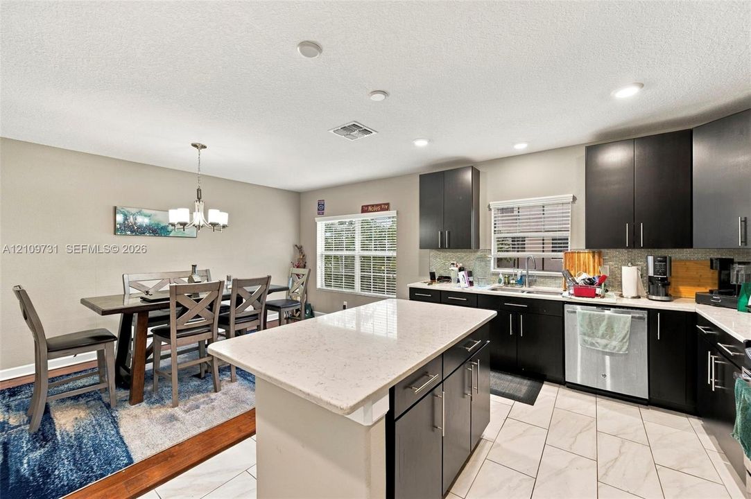 Kitchen featuring dark cabinetry, stone-finish countertops, a central island, stainless steel dishwasher, and ceramic tile flooring