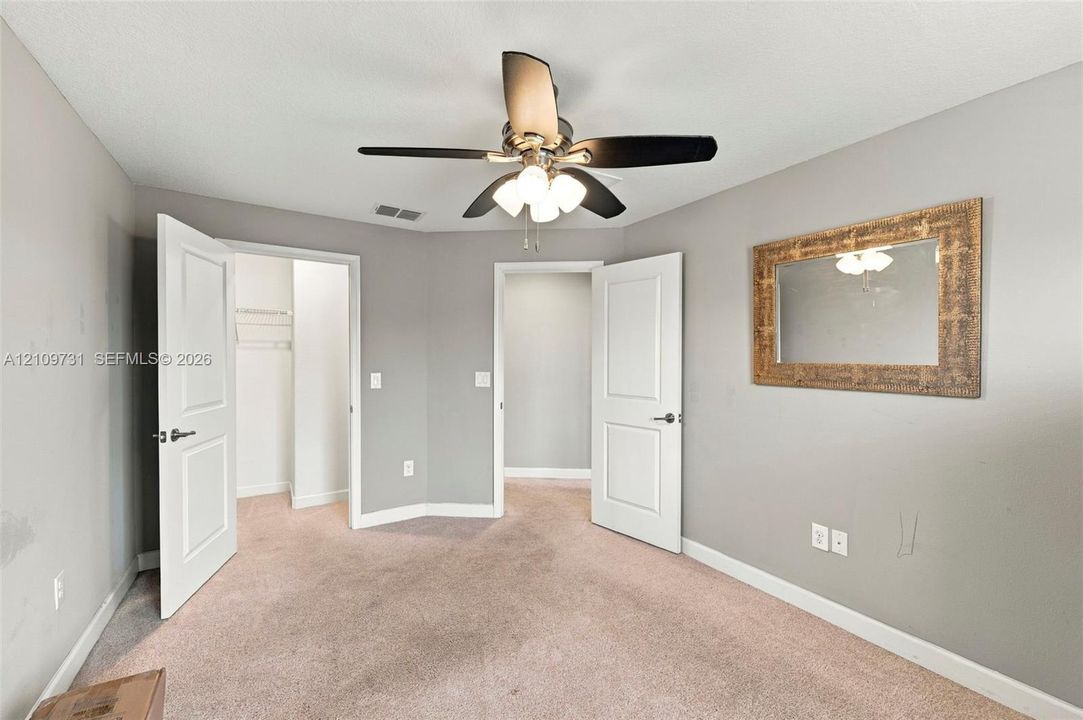 Neutral-toned interior space featuring carpeting, a multi-light ceiling fan, and two-panel doors