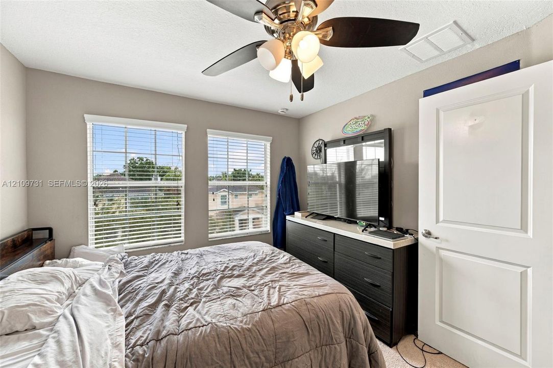 Neutral-toned interior featuring dual windows with horizontal blinds, a ceiling fan with integrated lighting, and a solid-core panel door