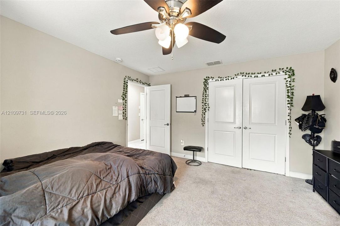 Neutral-toned room featuring neutral wall-to-wall carpeting, a multi-blade ceiling fan with integrated lighting, and white interior doors with two-panel detailing