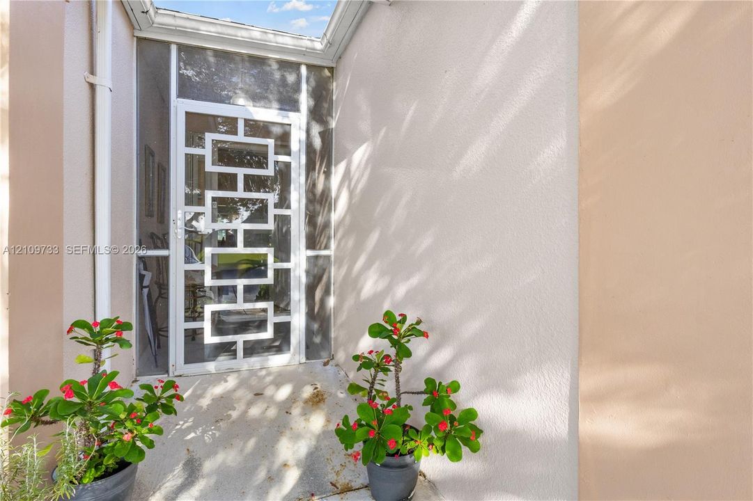 Entrance featuring a white geometric-pattern security door, clear glass sidelights, smooth stucco exterior finish, and overhead skylight