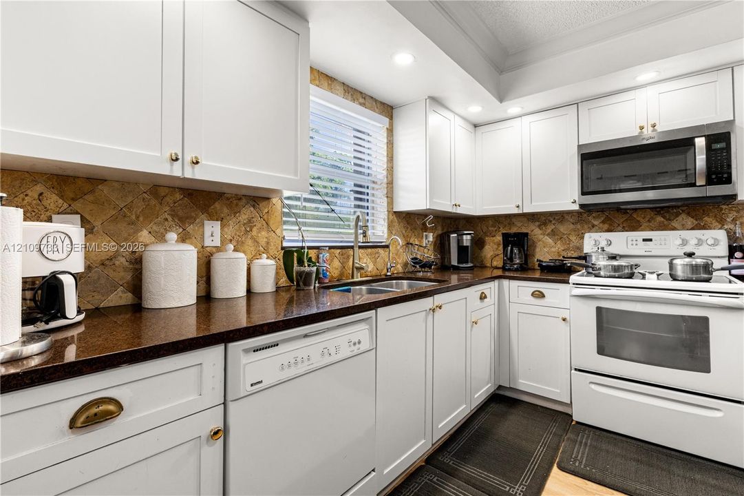 Kitchen featuring white cabinetry, stone-finish countertops, diagonal-set stone backsplash, recessed lighting, and stainless steel microwave