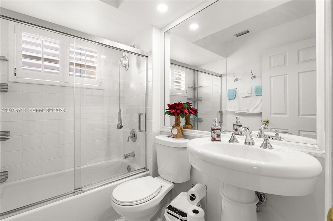 Bathroom featuring a shower-tub combination with a sliding glass door, white wall tiling, a pedestal sink with polished chrome fixtures, and a large-format mirror