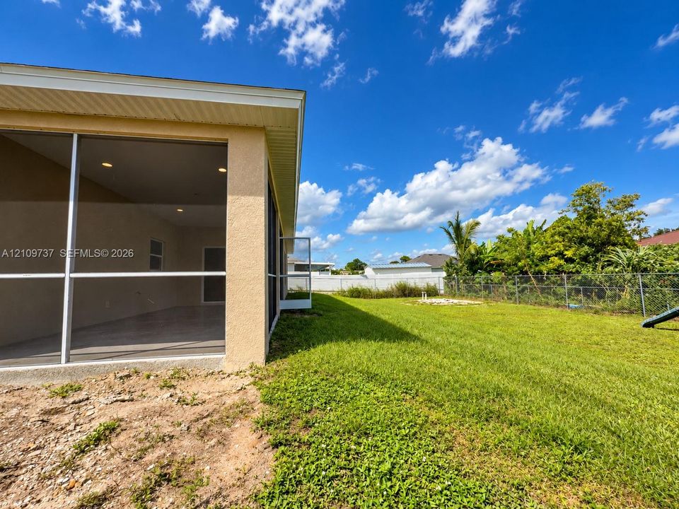 Stucco-finished exterior with a screened-in covered lanai featuring recessed lighting, a grass lawn, and chain-link perimeter fencing