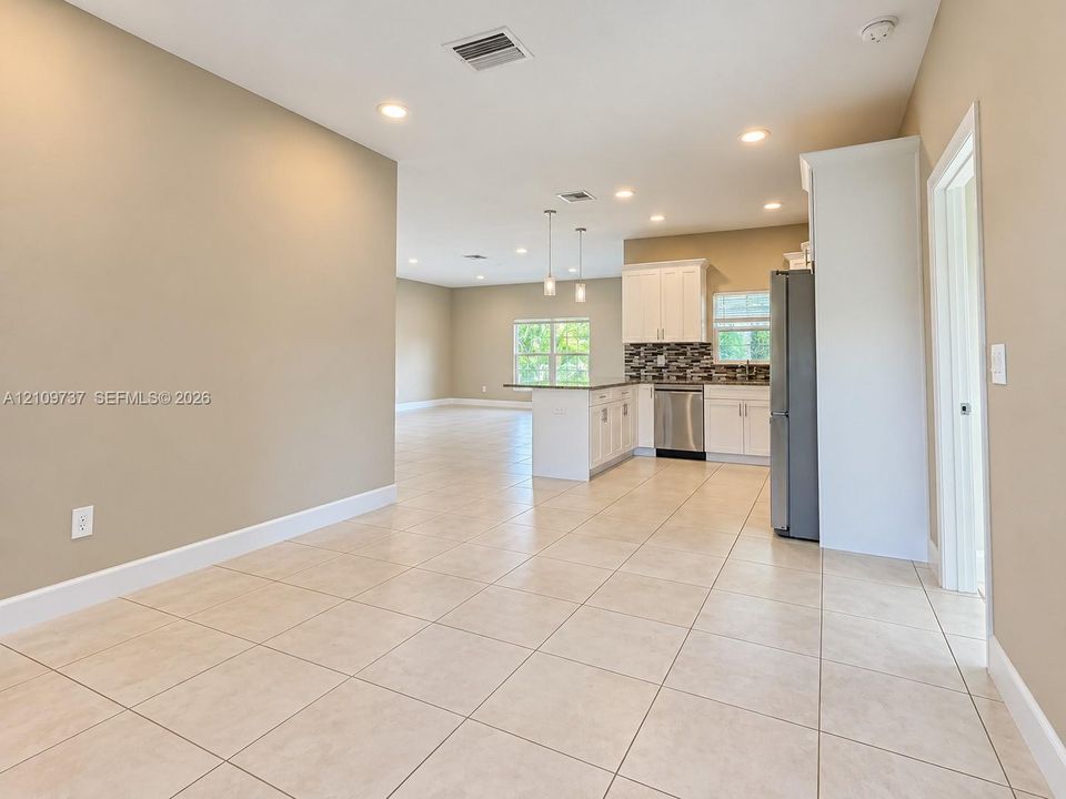 Kitchen featuring white cabinetry, a peninsula with stone-finish countertops, stainless steel appliances, a multi-tonal tile backsplash, and ceramic tile flooring