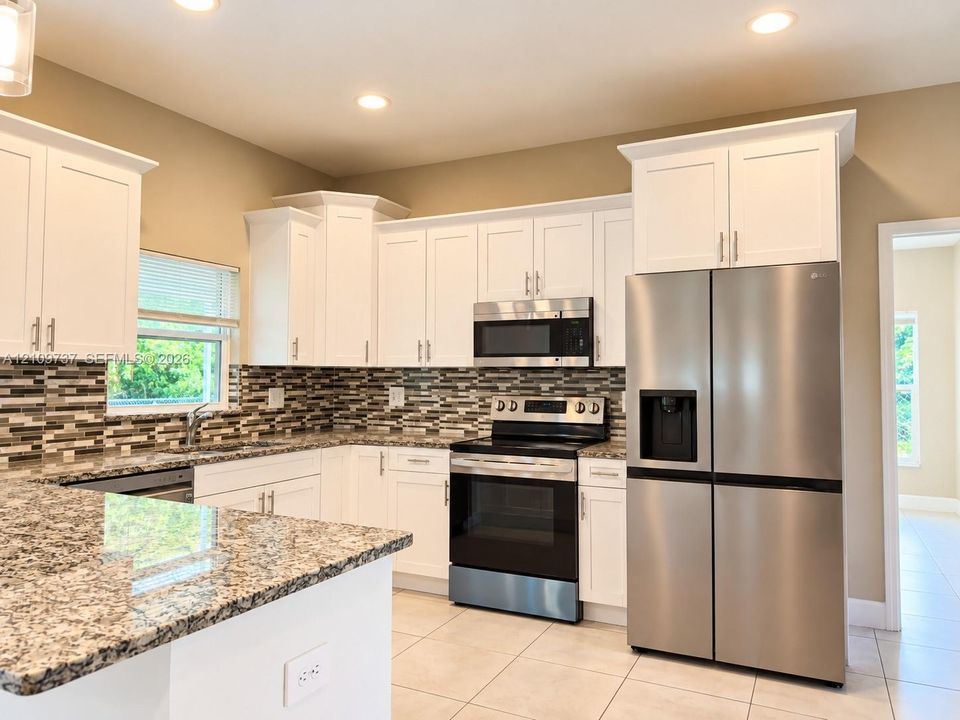 Kitchen featuring white cabinetry with crown molding, stone-patterned countertops, a multi-tonal linear tile backsplash, and stainless steel appliances
