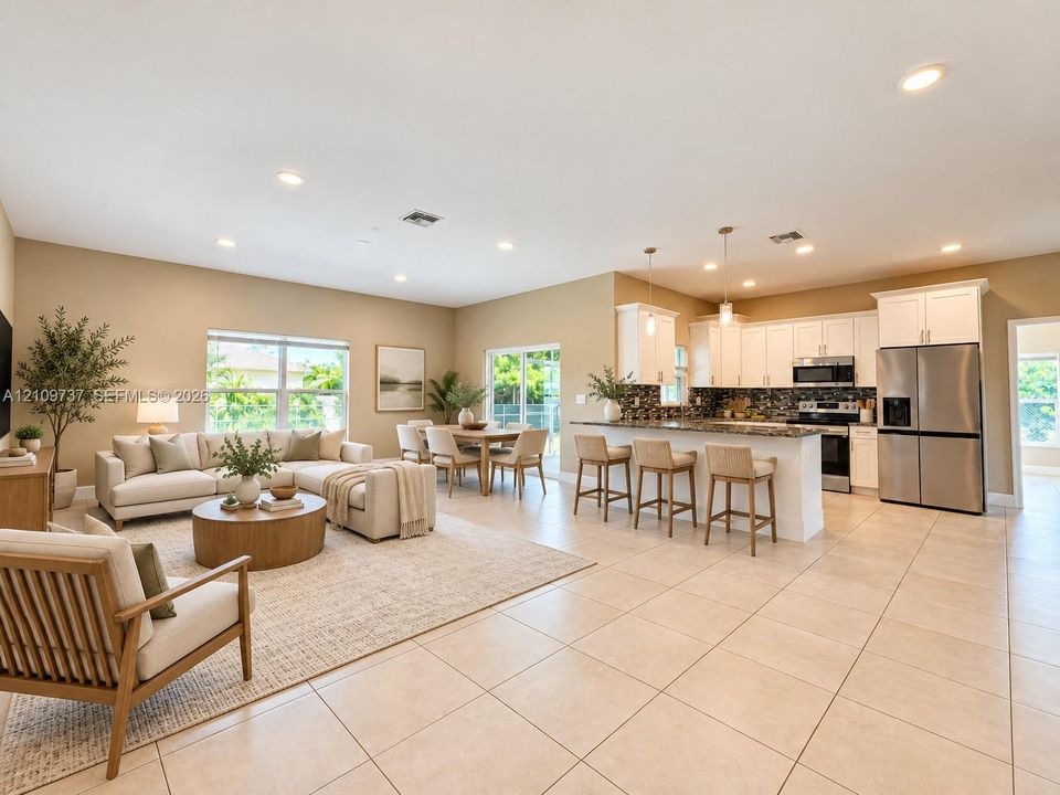 Open-concept interior featuring light tile flooring, recessed lighting, white kitchen cabinetry, stainless steel appliances, and a kitchen island with bar seating