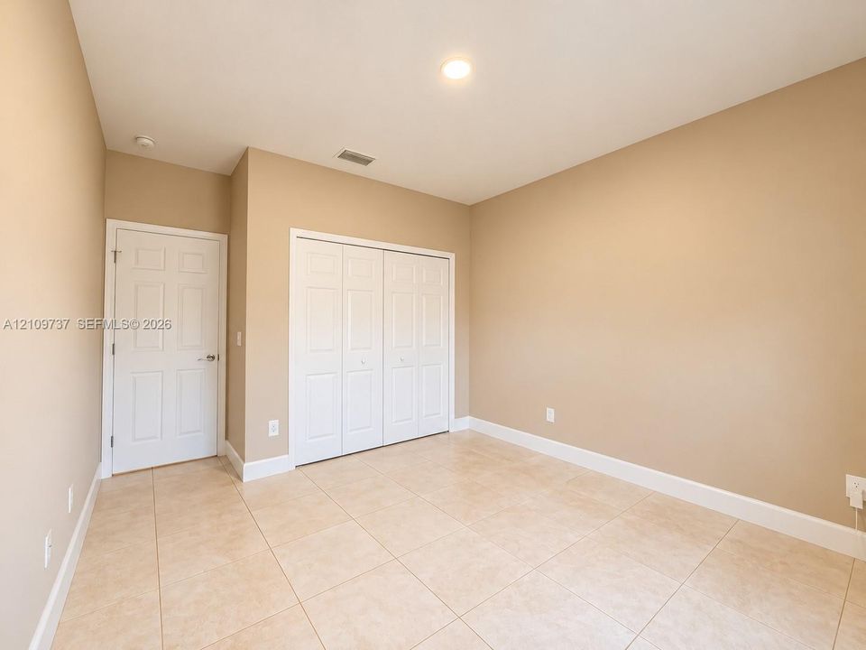 Room featuring light-toned tile flooring, neutral wall paint, and a built-in double-door closet with a separate paneled door