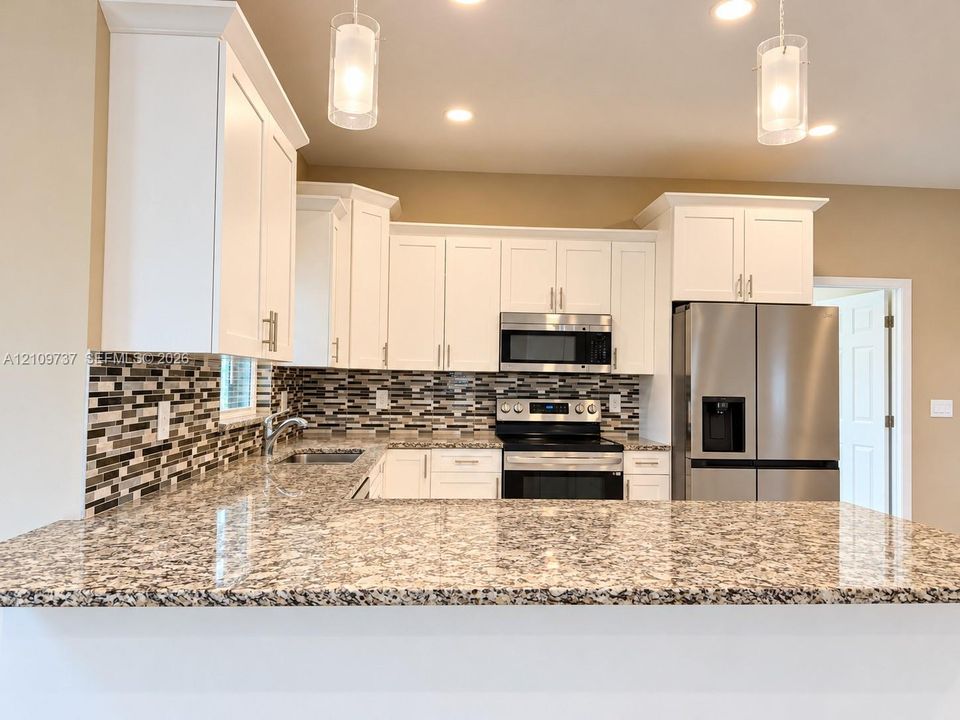 Kitchen featuring white cabinetry, stone-patterned countertops, a multi-tone tile backsplash, stainless steel appliances, and pendant lighting