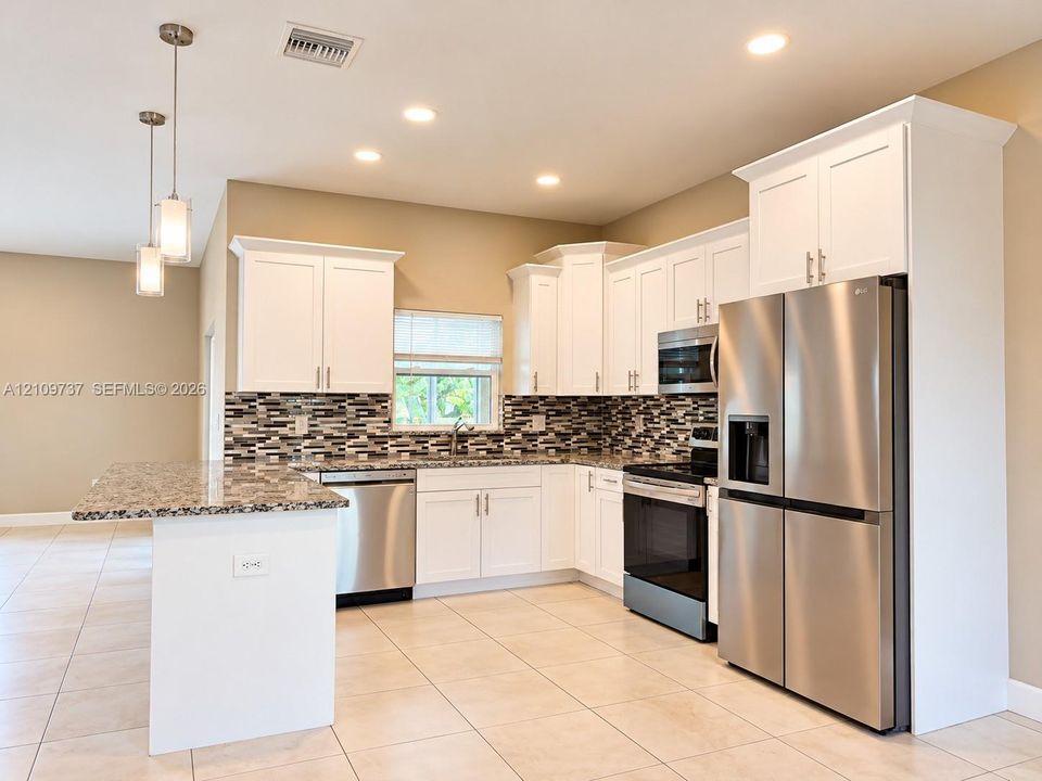 Kitchen featuring white cabinetry, stone-finish countertops, stainless steel appliances, a tile backsplash, and dual pendant lighting