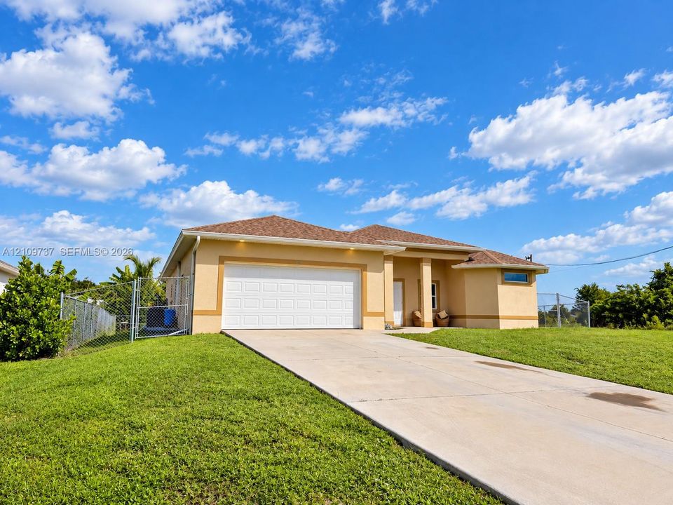 Stucco exterior residence featuring a concrete driveway, two-car garage, hip roof, and surrounding chain-link fencing