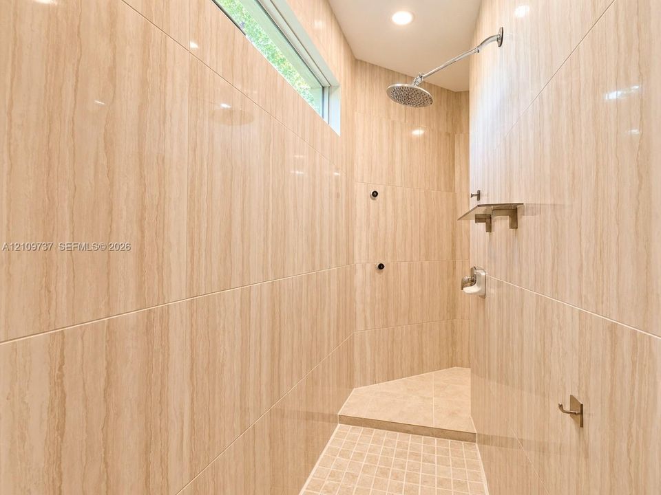 Walk-in shower featuring floor-to-ceiling stone-finish wall tile, a recessed transom window, a rainfall showerhead, a built-in stone shelf, and a mosaic tile shower floor
