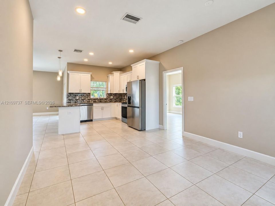 Kitchen featuring white cabinetry, a stone-finish tile backsplash, stainless steel appliances, a peninsula with stone-finish countertops, and light-tone floor tiling