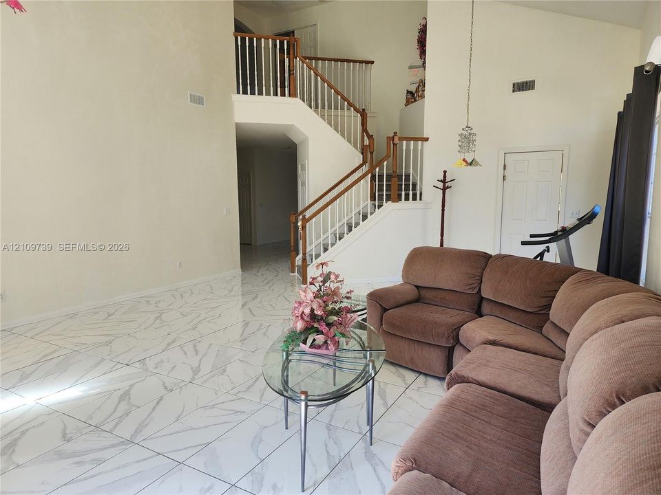 High-ceiling interior featuring large-format tile flooring with a veined pattern and a central staircase with wooden handrails and balusters