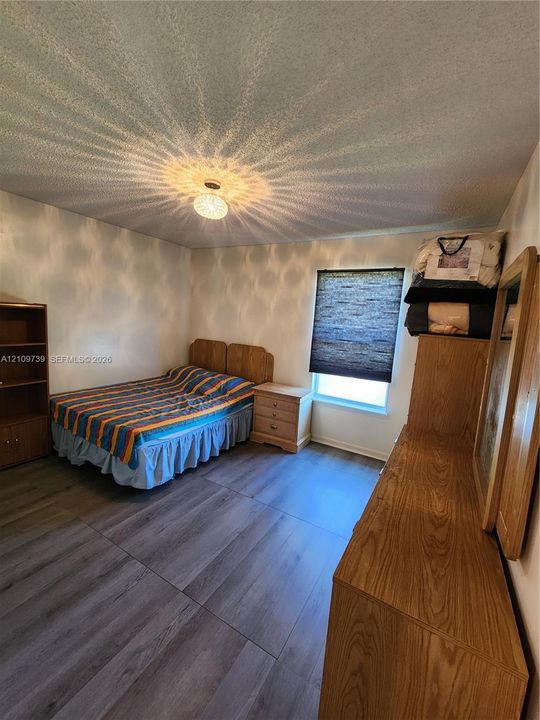 Wood-finish flooring, textured ceiling, central ceiling-mounted light fixture, and window with adjustable shade