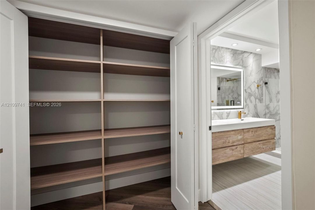 Built-in storage closet featuring wood-finish shelving, and bathroom with a floating wood-finish vanity, integrated rectangular sink, wall-mounted faucet, and stone-finish wall tile