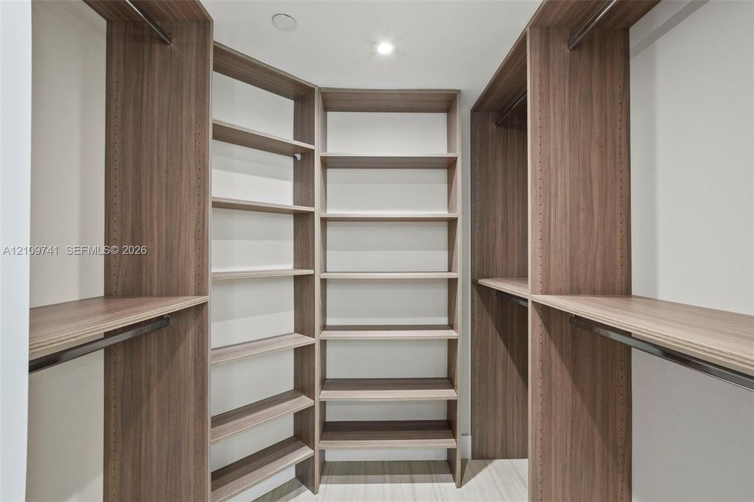 Custom walk-in closet featuring wood-finish cabinetry, built-in shelving units, integrated hanging rods, and recessed lighting