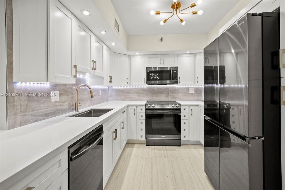 Kitchen featuring white shaker-style cabinetry, stainless steel appliances, stone-surface countertops, under-cabinet lighting, and wood-finish flooring