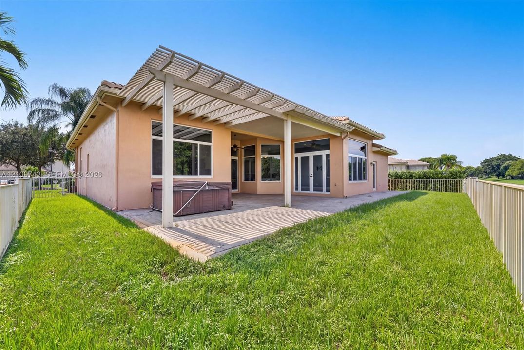 Stucco exterior featuring a covered patio, trellis-style roof extension, concrete hardscaping, and surrounding metal fencing