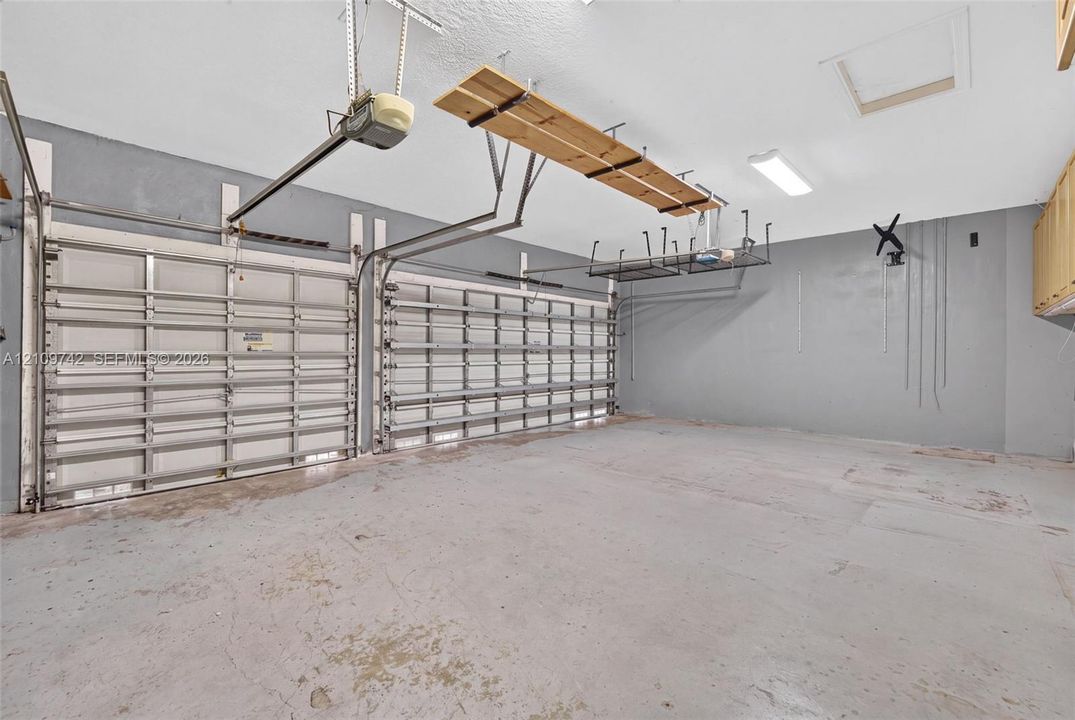Two-car garage featuring dual overhead metal doors, painted concrete flooring, ceiling-mounted storage racks, and built-in wall cabinetry