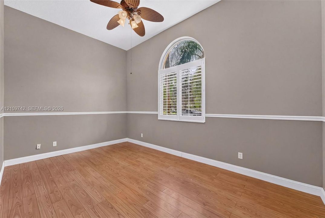 Room featuring wood-finish flooring, an arched window with plantation shutters, decorative chair rail molding, and a multi-blade ceiling fan