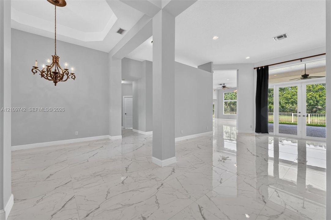 Interior featuring polished stone-finish tile flooring, a tray ceiling, an ornate metal chandelier, architectural support columns, and French doors