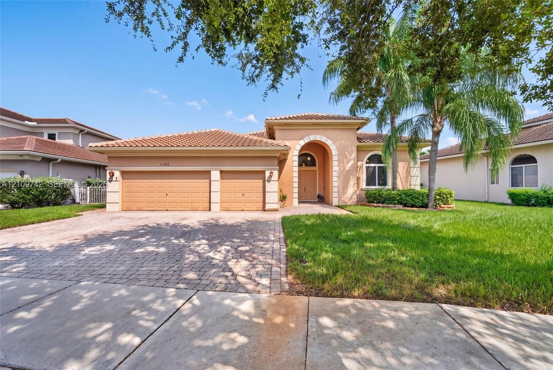 Stucco exterior with a tiled roof, arched entryway, two-car garage, and paver driveway