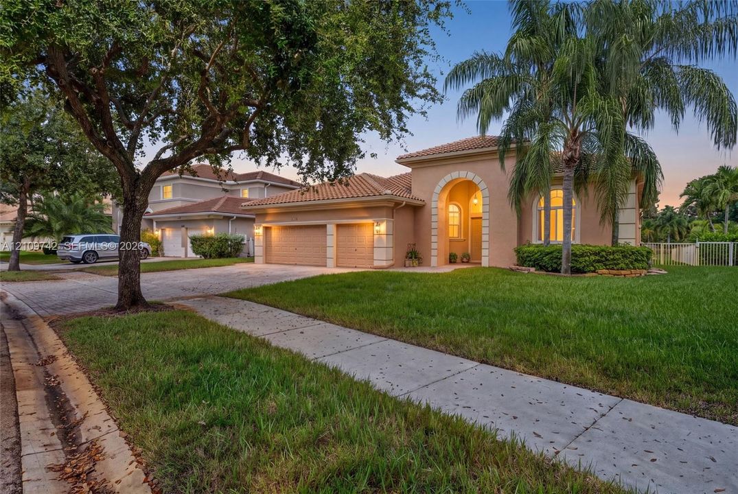 Stucco exterior featuring an arched entryway, tile roof, two-car garage, and paved driveway