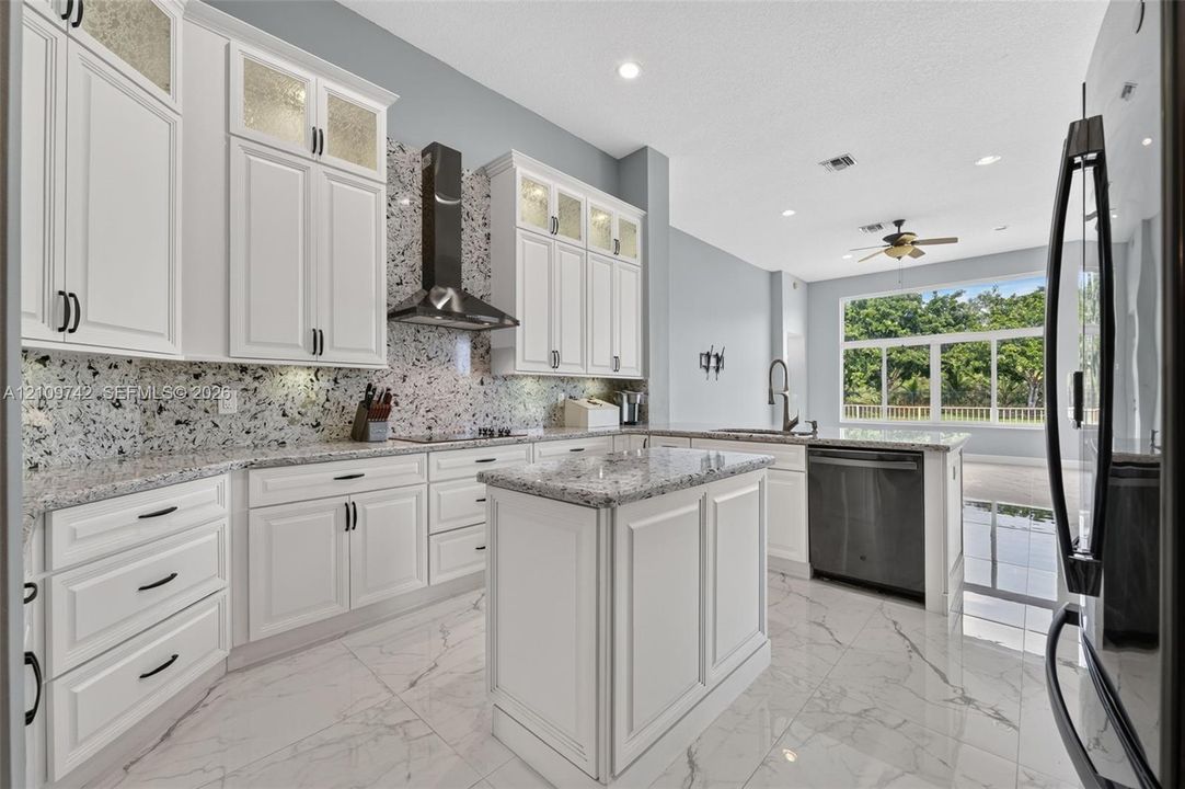 Kitchen featuring white cabinetry with glass-panel upper doors, stone-finish countertops, full-height decorative backsplash, stainless steel range hood, and large-format tile flooring