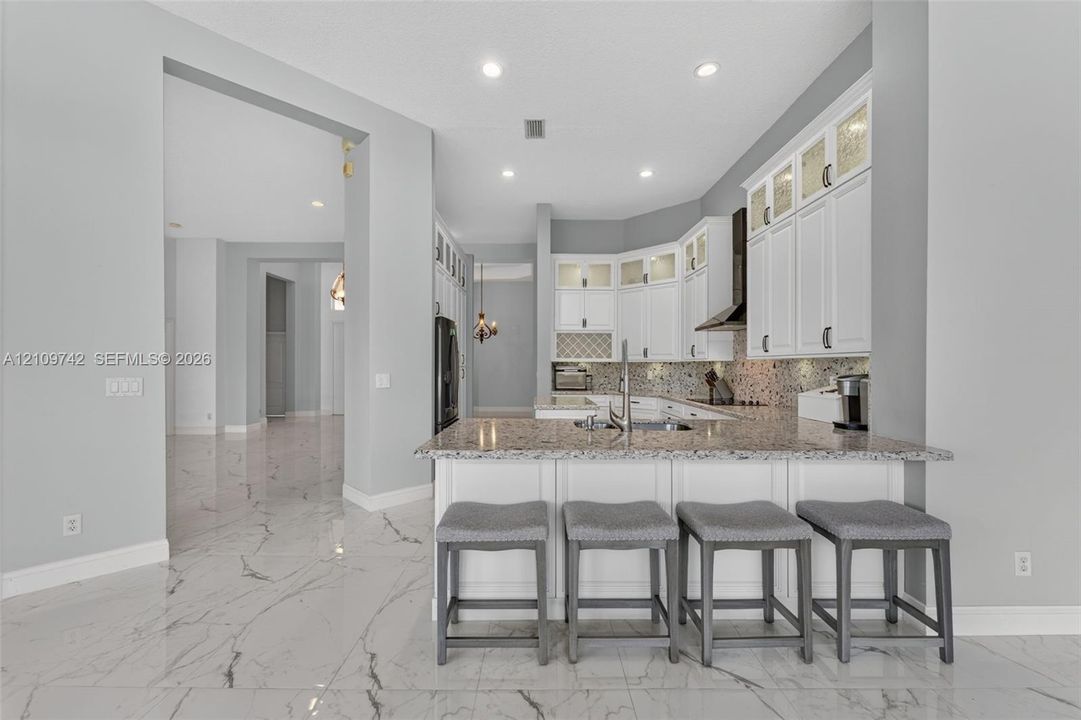 Kitchen featuring white cabinetry with glass-front uppers, stone-patterned countertops, a stainless steel undermount sink, recessed ceiling lighting, and large-format polished tile flooring