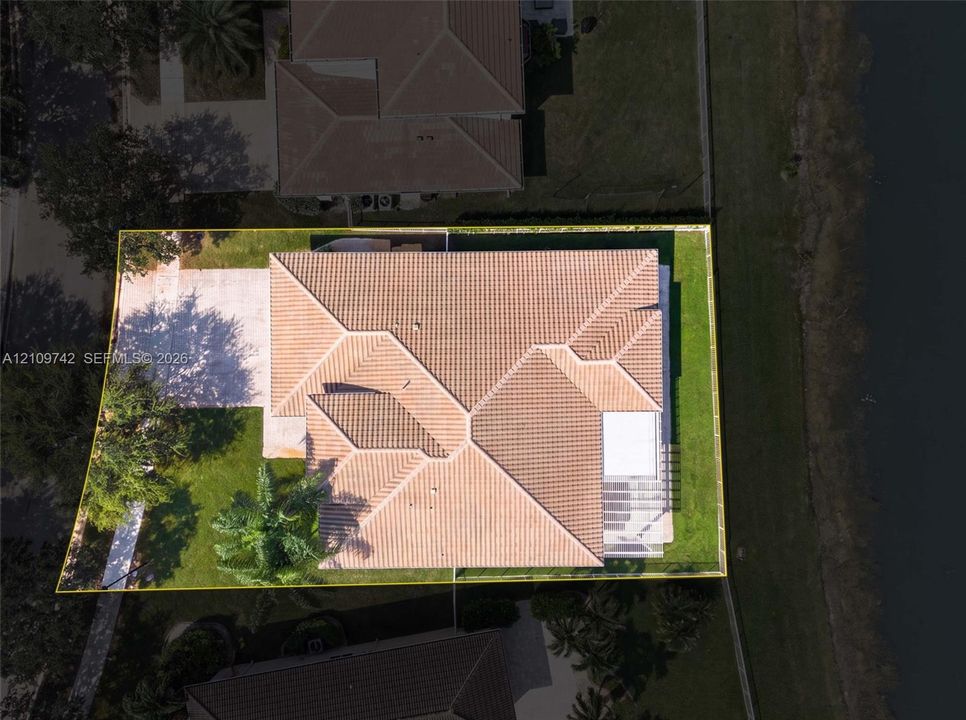Aerial perspective of a property featuring a tile roof, concrete driveway, and a fenced yard with perimeter landscaping