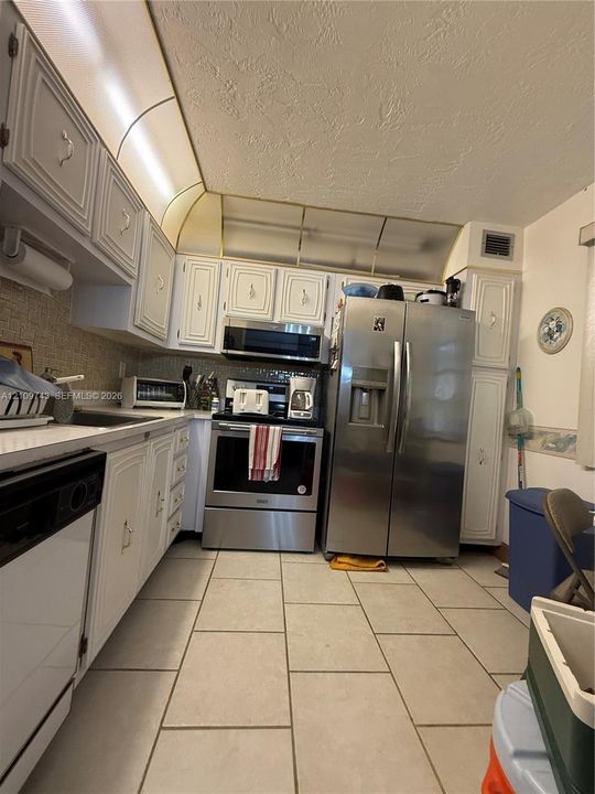 Kitchen featuring white cabinetry, stainless steel appliances, ceramic tile flooring, and integrated overhead lighting