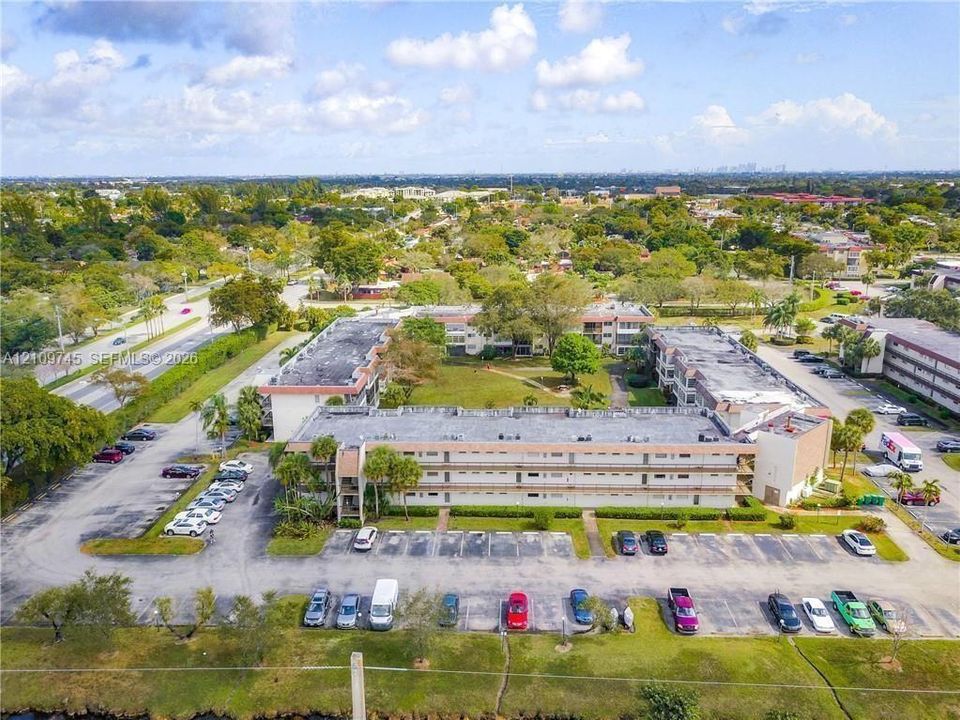 Aerial perspective of a multi-story residential complex featuring low-rise architectural design, expansive on-site surface parking, and manicured green spaces