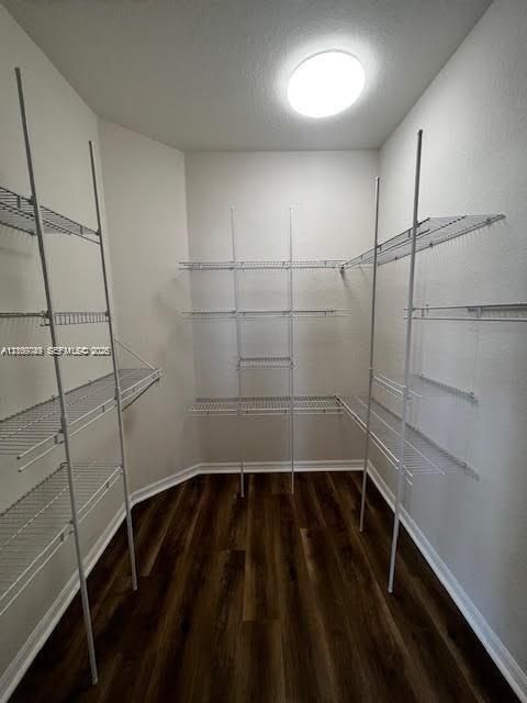 Storage area featuring floor-to-ceiling white wire shelving, wood-finish flooring, and a flush-mount ceiling light fixture