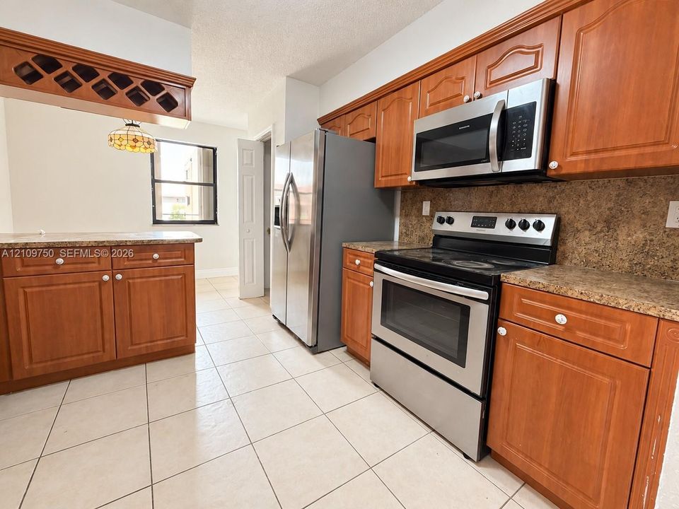 Kitchen featuring wood cabinetry, stainless steel appliances, speckled stone-finish countertops, tile flooring, and a built-in wine rack