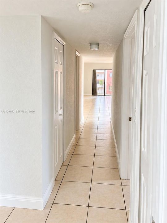 Hallway featuring neutral-toned tile flooring, multi-panel doors, and ceiling-mounted lighting fixtures