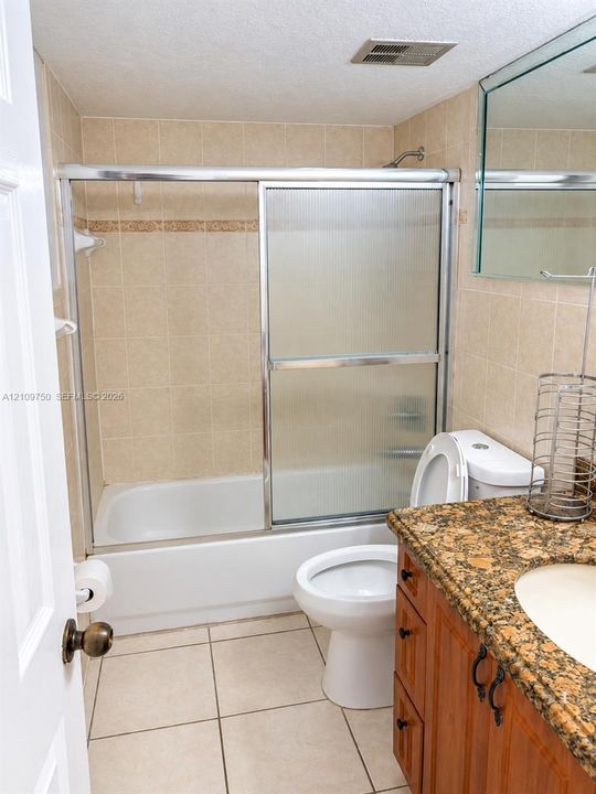 Bathroom featuring tile flooring, stone-surfaced vanity with wooden cabinetry, and a shower-tub combination with sliding glass doors