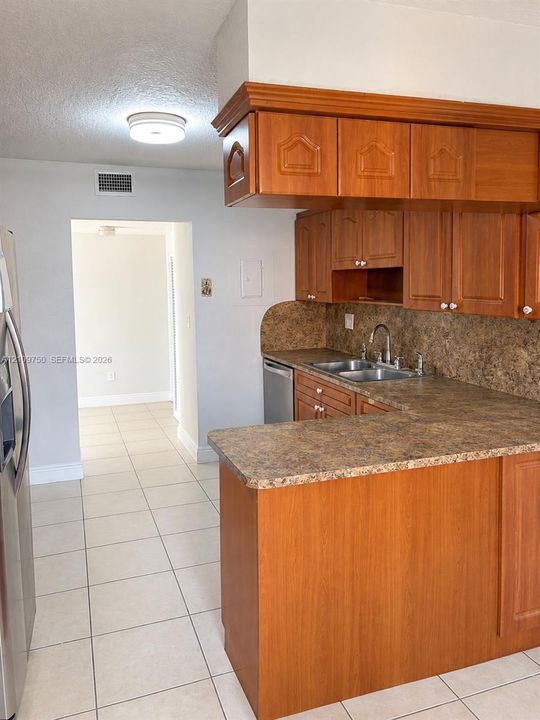 Kitchen featuring wood cabinetry, stone-finish countertops, stainless steel dual-basin sink with arched faucet, and tiled flooring