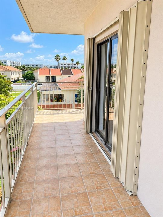 Covered balcony featuring tile flooring, metal railings, and accordion-style storm shutters