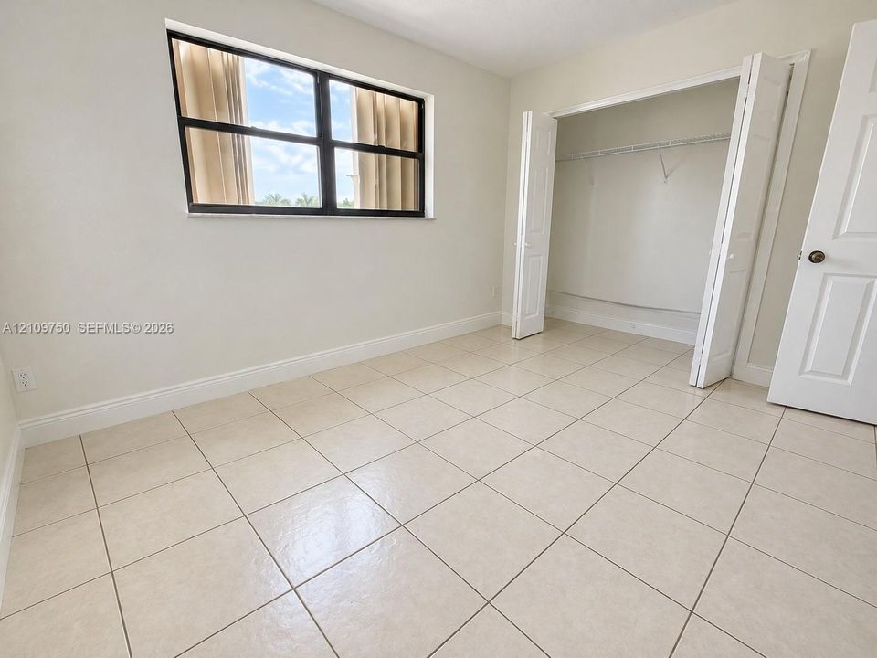 Neutral-toned ceramic tile flooring, horizontal sliding window with black frames, and bi-fold closet doors