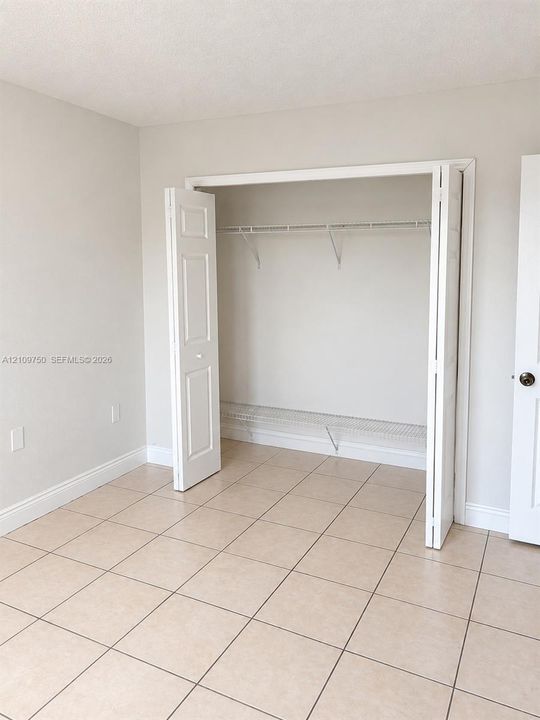 Neutral-toned wall finish, large-format tile flooring, and closet featuring dual bifold doors with white wire shelving