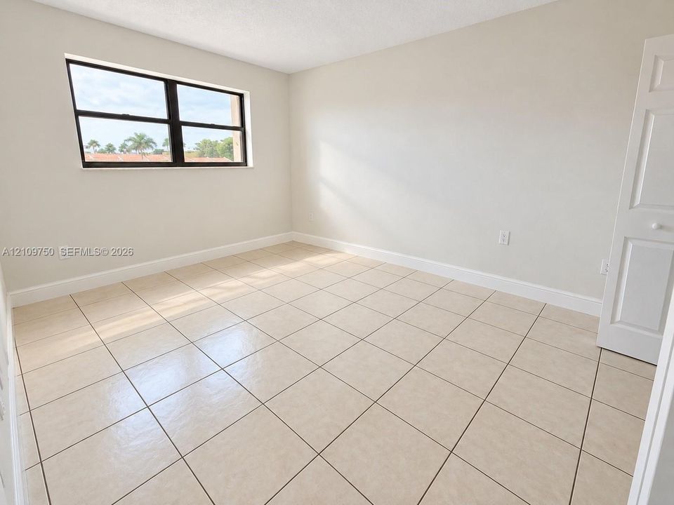 Neutral-toned room featuring large-format ceramic tile flooring, a multi-pane window with a black frame, and a white paneled closet door